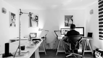 na zdjęciu znajduje się mężczyzna, który siedzi przed dwoma ekranami i pracuje na klawiaturze