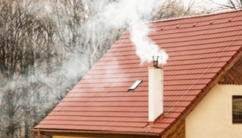 zdjęcie przedstawia kopcący białym dymem intensywnie komin na budynku jednorodzinnym pokrytym blachą