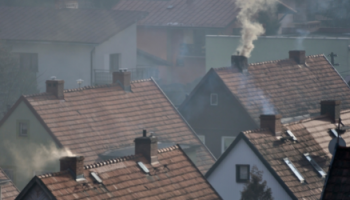 Dachy domów jednorodzinnych z kominami z których wydobywa się dym, który produkowany jest przez piece węglowe, tzw. kopciuchy