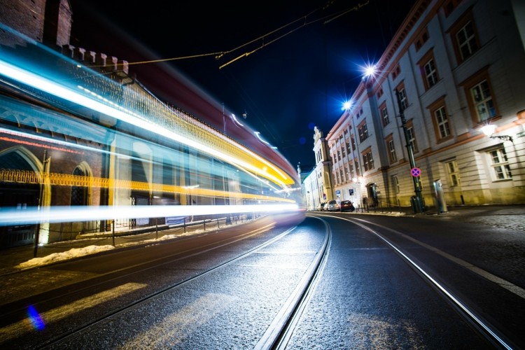 Na zdjęciu widać jedną z krakowskich ulic nocą. Na pierwszym tle znajdują się tory tramwajowe, którymi porusza się tramwaj