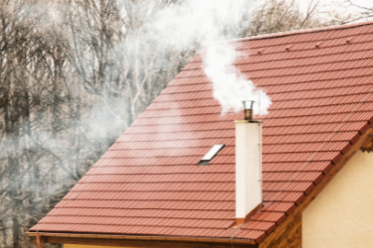 zdjęcie przedstawia kopcący białym dymem intensywnie komin na budynku jednorodzinnym pokrytym blachą
